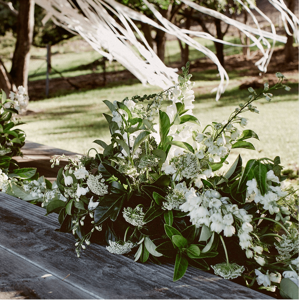 Outdoor wedding floral arrangement with white blooms and green foliage by Pippin, South Coast stylist.