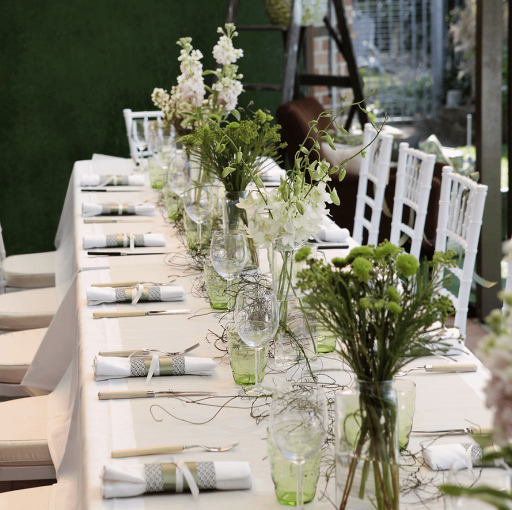 Elegant reception table styling with white chairs, glassware and seasonal flowers by South Coast event stylist Pippin.